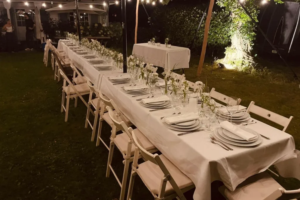 Lange gedeckte Hochzeitstafel mit hellen Stühlen und Blumendekoration